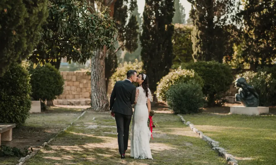 Ein Brautpaar küsst sich im Park. Die Braut trägt ein Spitzenkleid, der Bräutigam einen dunklen Anzug. Eine kroatische Hochzeit im Grünen.