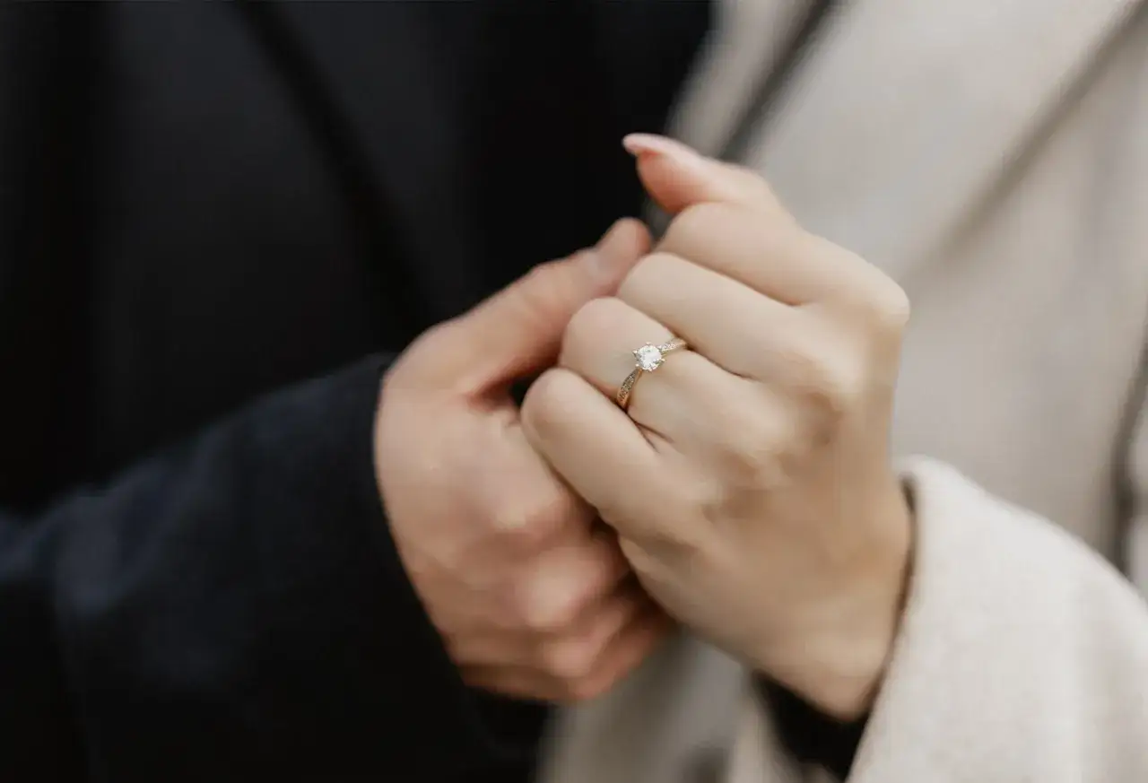 Ein Mann hält die Hand einer Frau, an deren Finger ein Verlobungsring funkelt. Die Geste symbolisiert die tiefe Bedeutung einer Verlobung und den Beginn eines gemeinsamen Lebens.