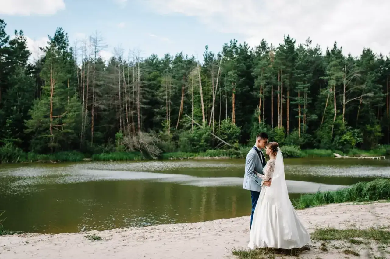 Ein Brautpaar genie&szlig;t den Moment am Ufer eines Sees. Die Hochzeit am See ist von einem dichten Wald umgeben.