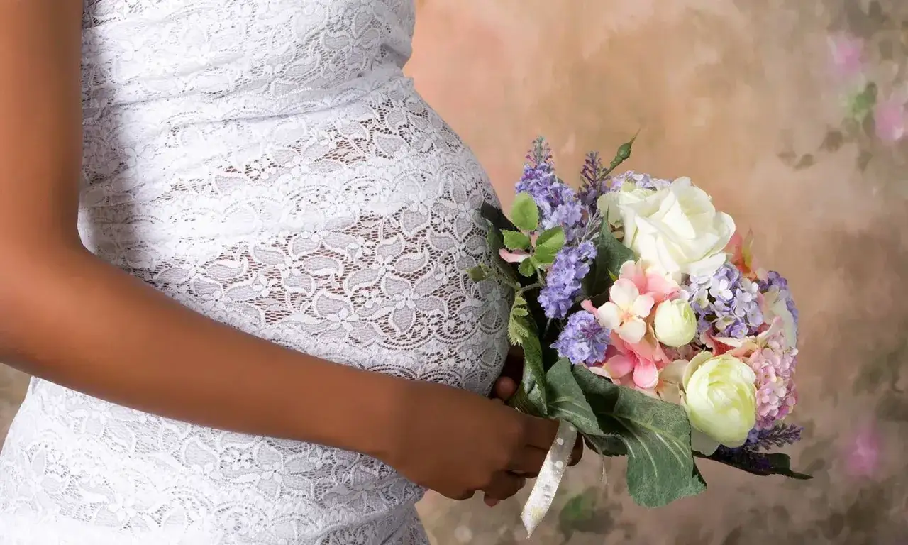 Schwanger heiraten: Eine Frau im wei&szlig;en Spitzenkleid h&auml;lt einen Blumenstrau&szlig;.