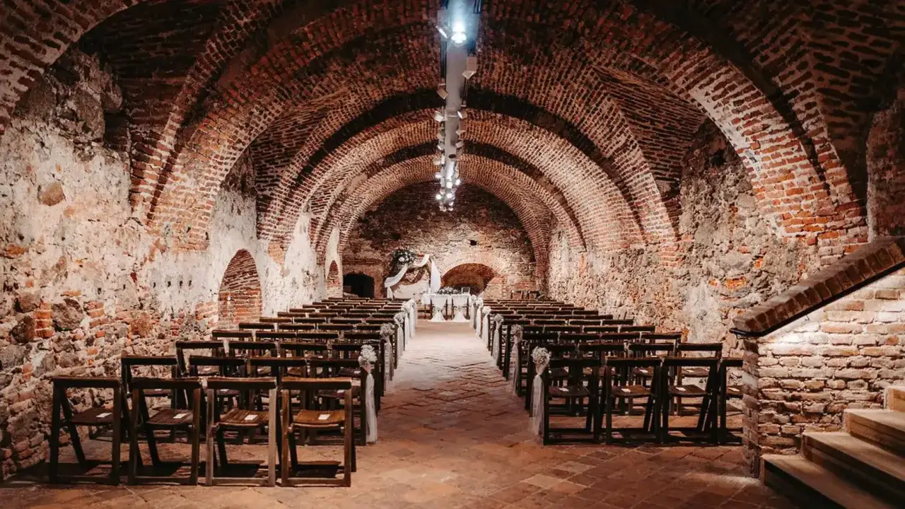 Einzigartige Location f&uuml;r eine unkonventionelle Hochzeit: Reihen von Holzst&uuml;hlen s&auml;umen einen Gang unter einem Ziegelsteingew&ouml;lbe, mit einem Altar am Ende.