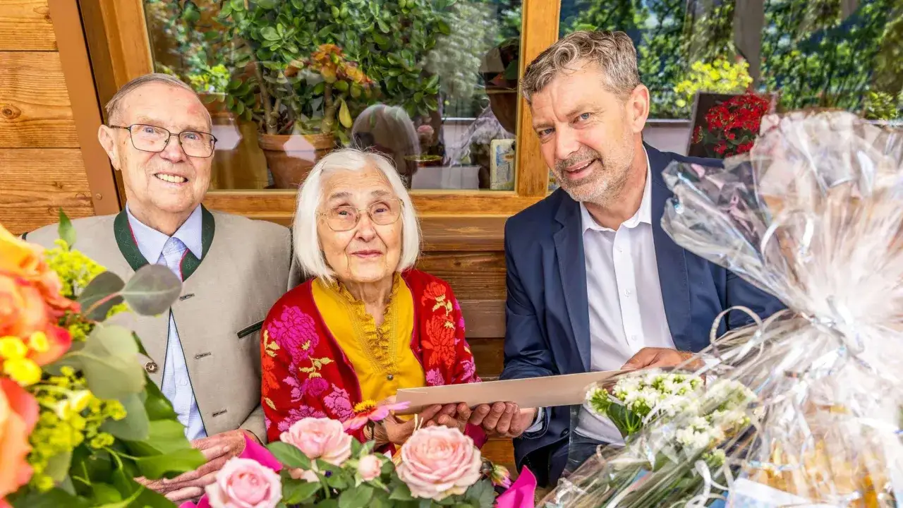 Ein &auml;lteres Paar feiert Gnadenhochzeit, wieviel Jahre sie wohl verheiratet sind? Sie sitzen mit Blumen und Geschenken im Freien.