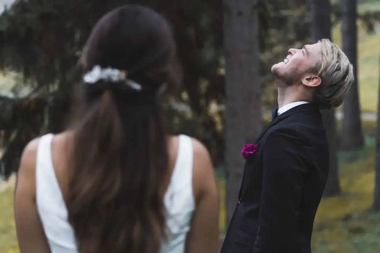 Ein Mann im Anzug lacht ausgelassen in den Himmel, w&auml;hrend eine Braut ihm den R&uuml;cken zukehrt. Vielleicht ist es die Angst vor der Hochzeit, die ihn so befreit?