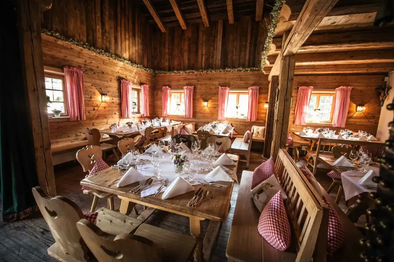 Gem&uuml;tliche Holzh&uuml;tte, festlich gedeckte Tische f&uuml;r eine Egerner Alm Hochzeit. Rote Karovorh&auml;nge und Blumen schm&uuml;cken den rustikalen Raum.