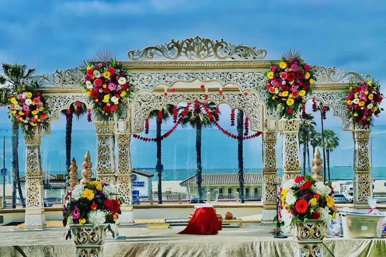 Prachtvoller Mandap f&uuml;r eine Bollywood-Hochzeit am Strand, geschm&uuml;ckt mit bunten Blumen und Palmen im Hintergrund.