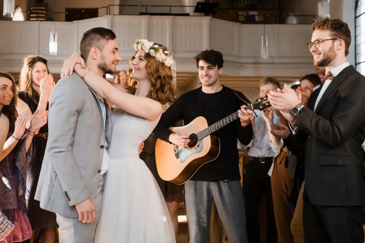 Ein Brautpaar tanzt, w&auml;hrend ein Mann Gitarre spielt und G&auml;ste klatschen. Die Stimmung ist fr&ouml;hlich, passend zu den Hochzeitsliedern auf Deutsch.