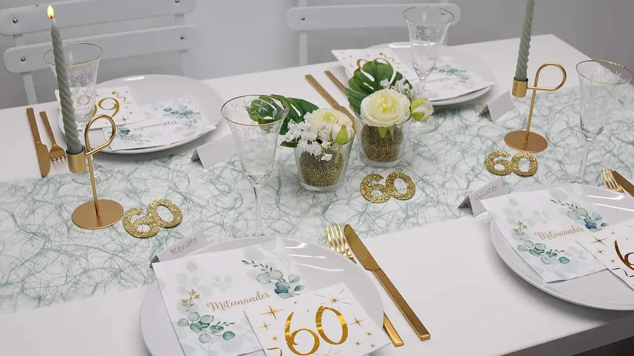 Festlich gedeckter Tisch f&uuml;r eine 60. Geburtstagsfeier. Goldene Kerzenhalter, Gl&auml;ser und Besteck. Kleine Blumenarrangements und 