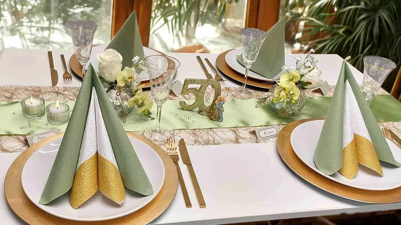 Festlich gedeckter Tisch f&uuml;r eine 50. Hochzeitstag. Das beste am verheiratet sein ist, gemeinsame Meilensteine zu feiern. Goldene Teller, gr&uuml;ne Servietten, Kerzen und eine kleine Tanzfigur.