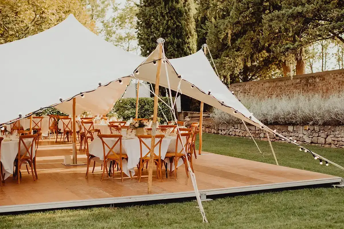 Festlich gedeckte Tische unter einem wei&szlig;en Zelt, bereit f&uuml;r eine Hochzeit. Lichterketten spannen sich &uuml;ber das Dach, als Schutz vor m&ouml;glichem Hochzeit Regen.