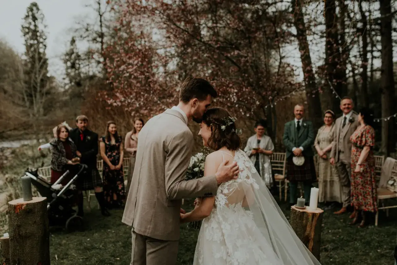Ein Brautpaar küsst sich bei einer romantischen veganen Hochzeit im Freien. Gäste stehen im Hintergrund.