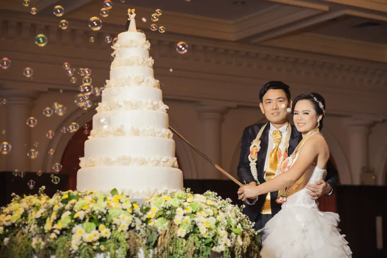 Ein Brautpaar feiert seine chinesische Hochzeit und schneidet gemeinsam die mehrst&ouml;ckige Torte an, w&auml;hrend Seifenblasen durch die Luft schweben.