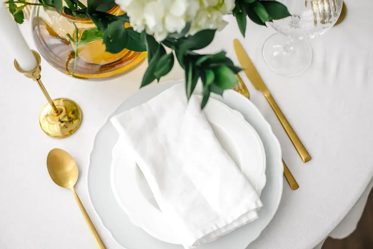 Festlich gedeckter Tisch für eine goldene Hochzeit im kleinen Kreis. Weiße Stoffserviette auf Tellern, goldene Löffel und Messer, Kerzenhalter und Blumen.