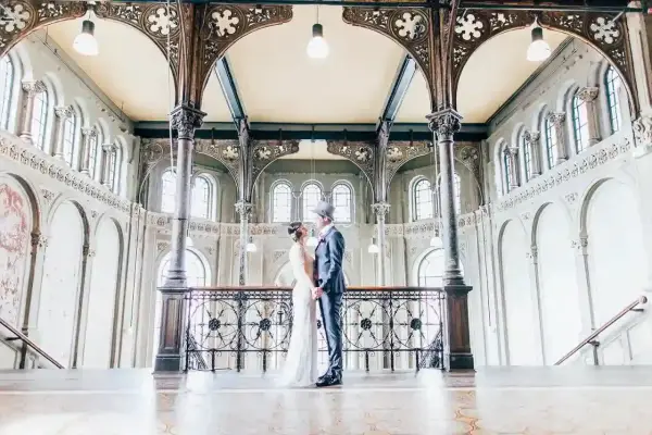 Ein Brautpaar im Stil der 20er Jahre steht sich in einem prachtvollen Gebäude mit Jugendstil-Architektur gegenüber.