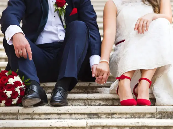 Brautpaar hält Händchen, rote Rosen und rote Schuhe. Die Frage "wie kurzfristig kann man heiraten" beschäftigt viele Paare.