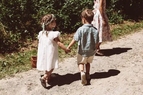 Zwei Kinder, ein Mädchen mit Blumenkranz und ein Junge, halten Händchen auf dem Weg zu einer Hochzeit mit Kindern.