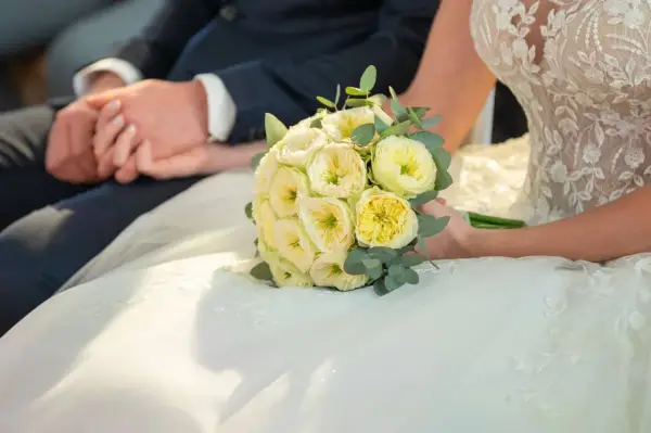 Brautpaar hält Händchen, Brautstrauß mit gelben Rosen. Eine Hochzeit Versicherung gibt Sicherheit für den großen Tag.